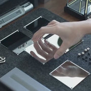 Assembly video for the INFINITY light showing hands assembling reflective metal components on a workspace.